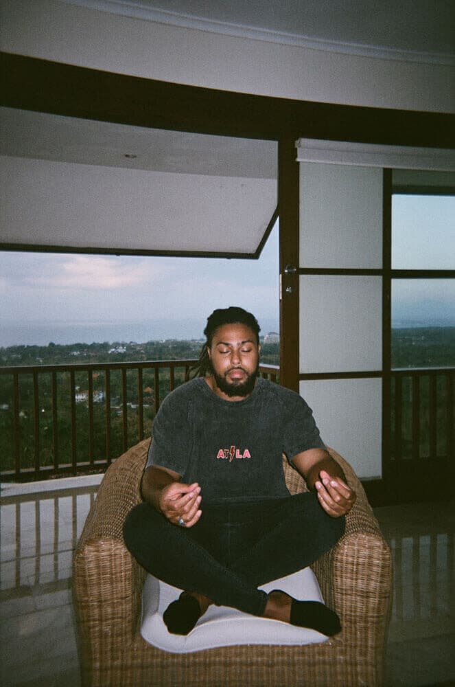 Corey meditating cross-legged on a balcony chair