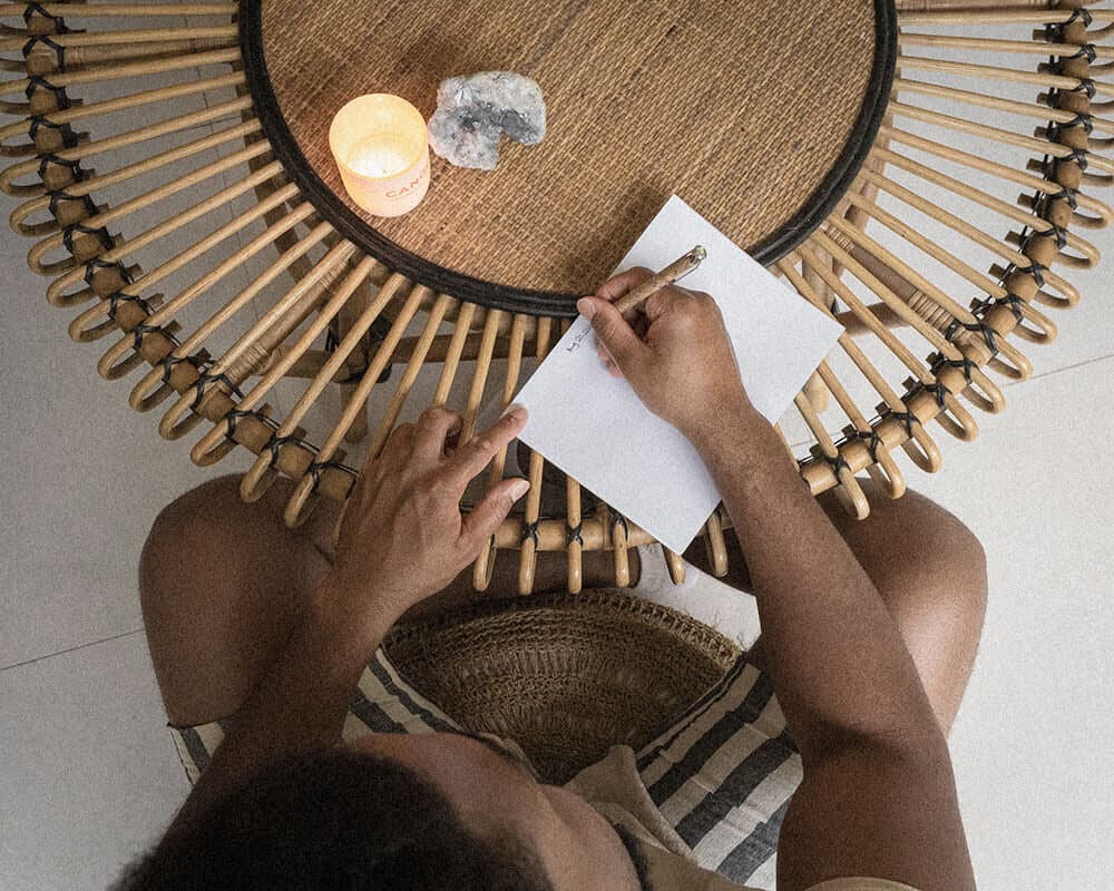 Corey’s hands writing in a notebook beside a candle, seen from above